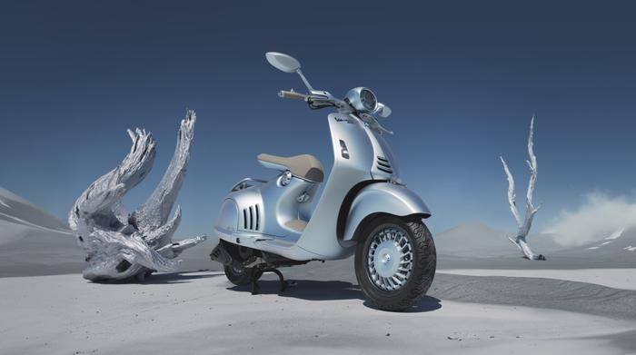 A sleek silver scooter parked on a desolate, sandy landscape with white mountains in the background and abstract white sculptures nearby, under a clear blue sky.