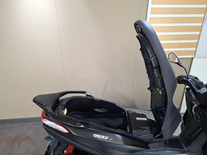 A black scooter with an open trunk, showcasing its storage compartment, against a neutral background.