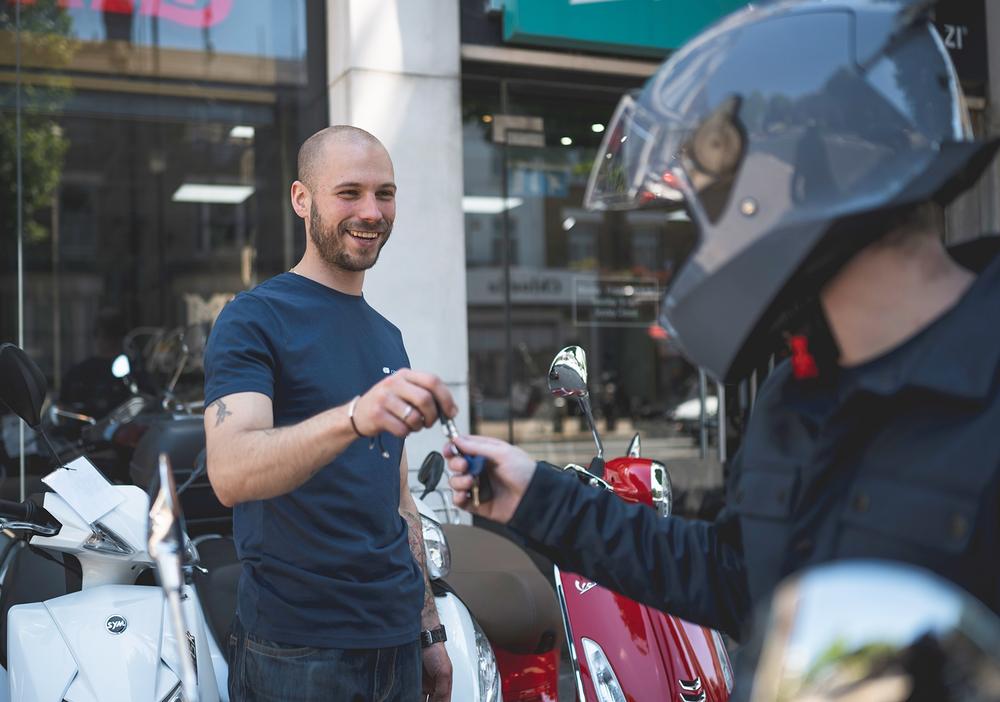 A Central Bikes salesman handing the keys of freedom to anther happy scooter commuter.