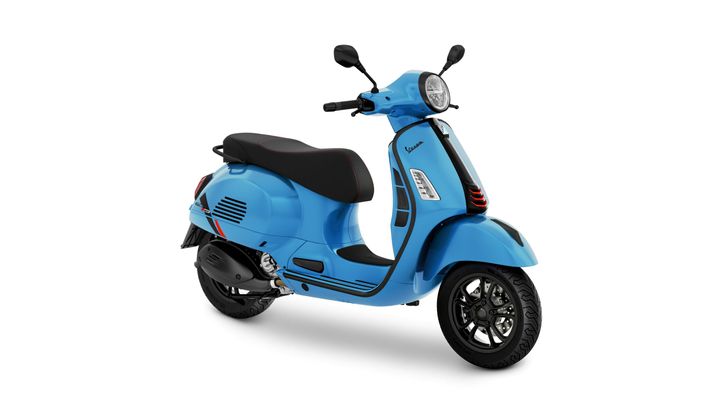 A stylish blue scooter with a retro design features a comfortable black seat, a round headlight, and sleek black wheels, positioned slightly at an angle.