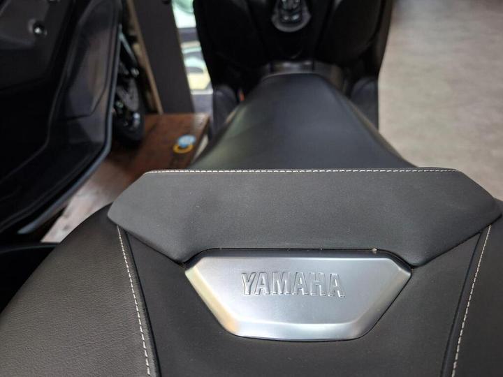 A close-up view of a motorcycle seat featuring a metallic Yamaha logo, with black leather and contrasting white stitching.