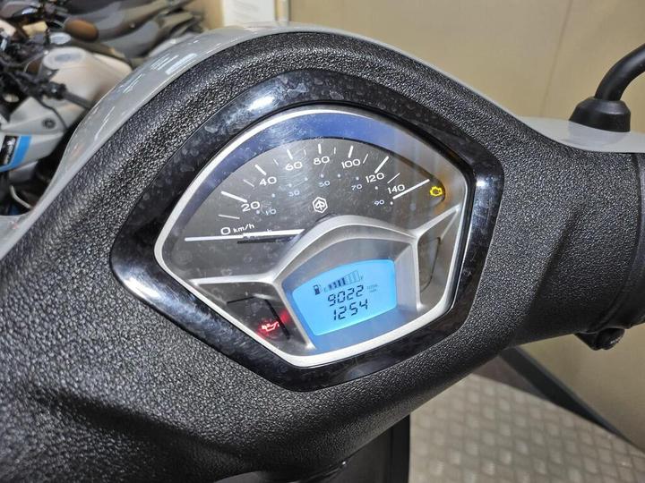 Close-up of a scooter dashboard displaying a speedometer, odometer reading 9,022 km, trip meter at 1,254 km, with indicator lights for oil and battery status.