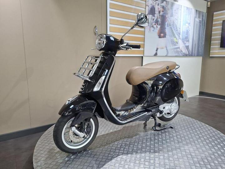 A sleek black scooter with a brown seat, showcased on a textured platform against a plain background and digital display.