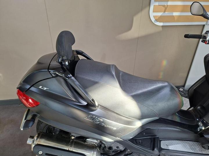 A close-up view of the seat and backrest of a black scooter, highlighting the sleek design and textured surface, with a blurred background.