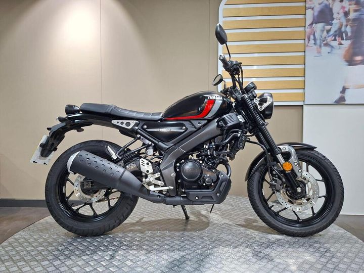 Yamaha XSR125 (2022) A sleek black and red Yamaha motorcycle is displayed on a textured surface in an indoor setting, showcasing its modern design and features.