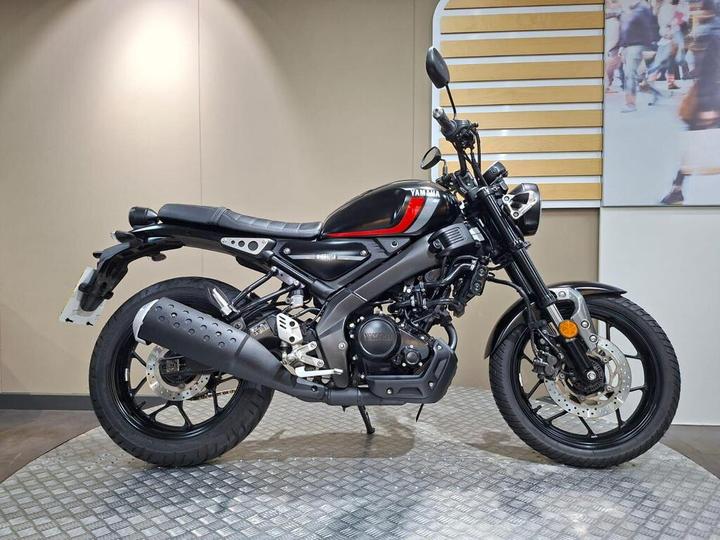 Yamaha XSR125 (2022) A sleek black and red Yamaha motorcycle is displayed on a textured surface in an indoor setting, showcasing its modern design and features.