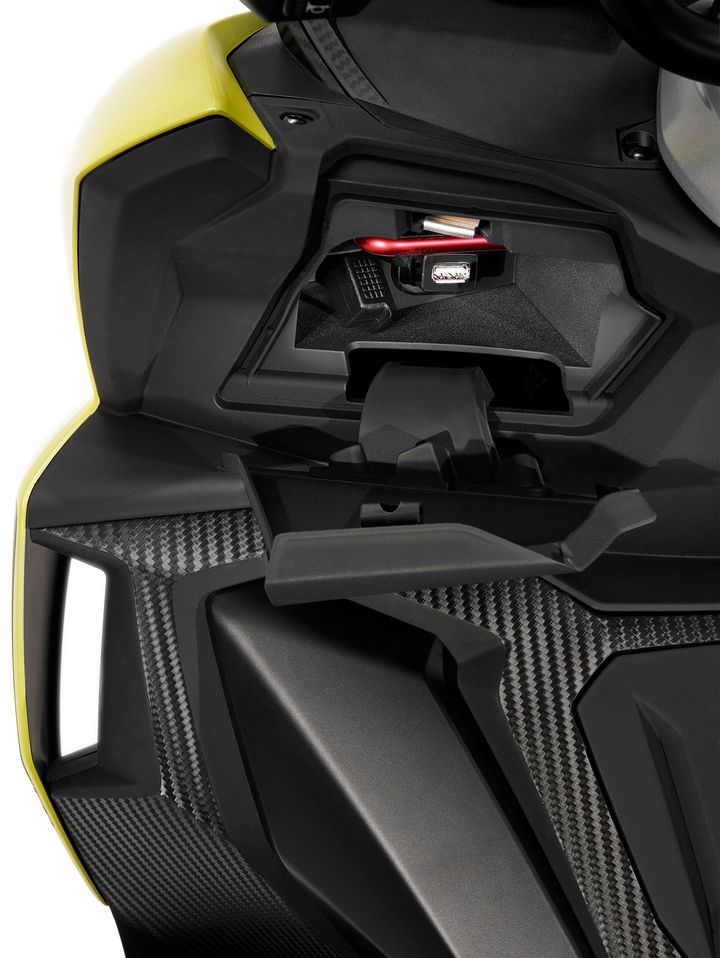 Close-up view of a motorcycle's upper bodywork with a focus on the storage compartment that features a red multi-tool and a reflective safety vest inside.