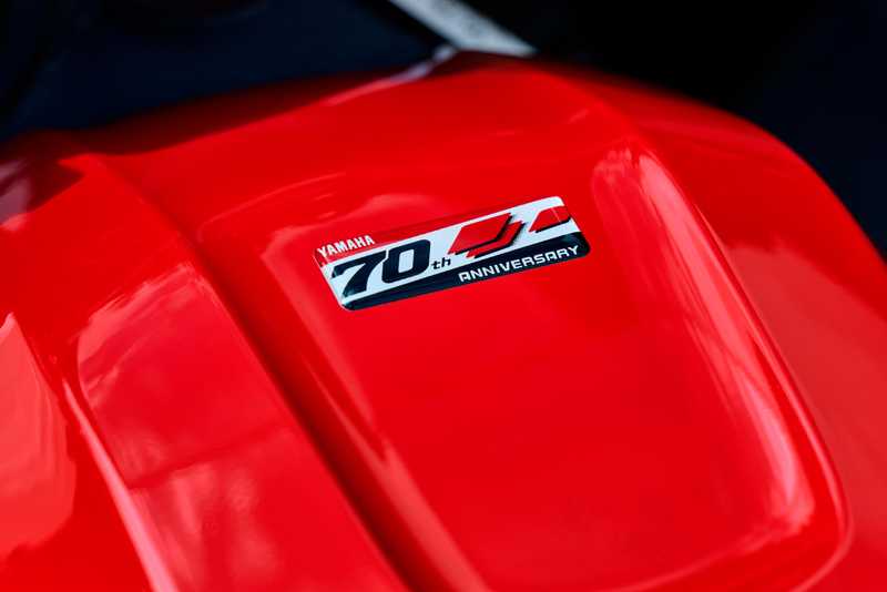 Close-up of a shiny red surface featuring a silver badge that reads "Yamaha 70th Anniversary."