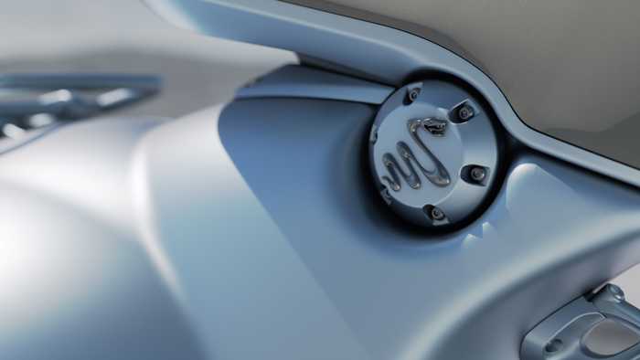 Close-up of a metallic motorcycle component, showcasing a circular fuel cap with detailed engravings and surrounding sleek, polished bodywork.