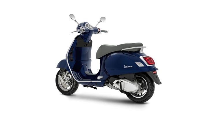 A blue Vespa scooter viewed from the rear, showcasing its sleek design, chrome details, and smooth lines against a white background.