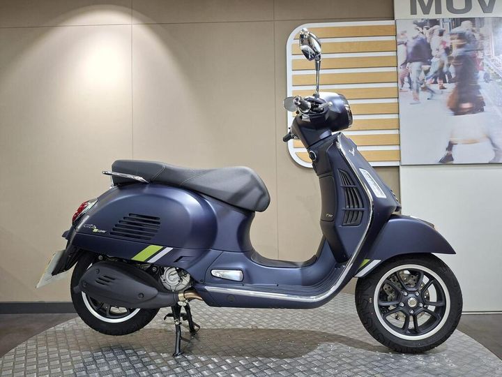 Vespa GTS 310 Supertech (2025) A blue Vespa scooter displayed against a neutral backdrop, featuring a sleek design with a prominent front headlight, stylish wheels, and a glossy finish.