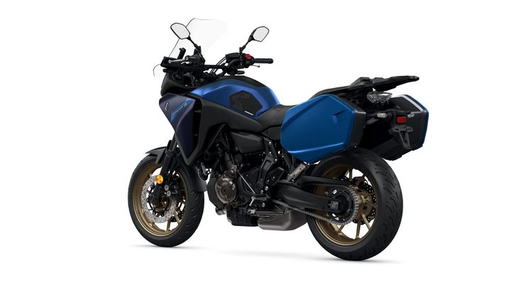 A blue adventure motorcycle with gold rims, side cases, and a rugged design, viewed from the rear left angle against a white background.