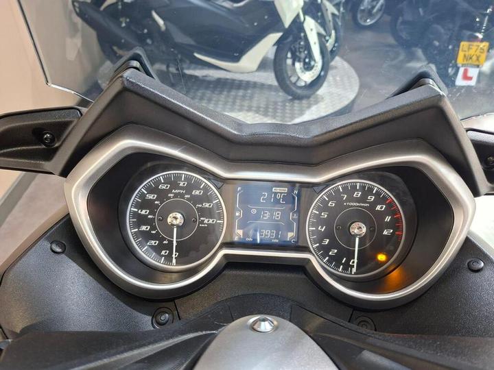 Close-up view of a motorcycle dashboard displaying a speedometer, tachometer, and digital readout with current temperature (21°C), time (13:18), and mileage (393.1 miles).