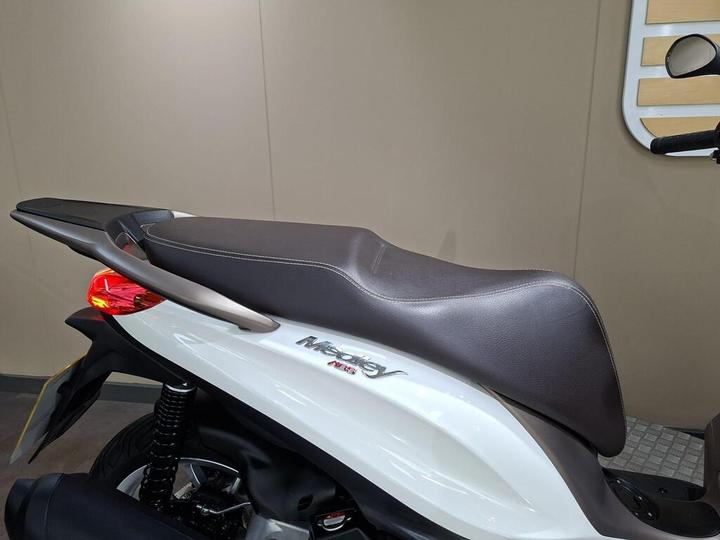 Close-up view of the seat of a white motorcycle with dark brown upholstery, showcasing the rear section and part of the body near the tail light.