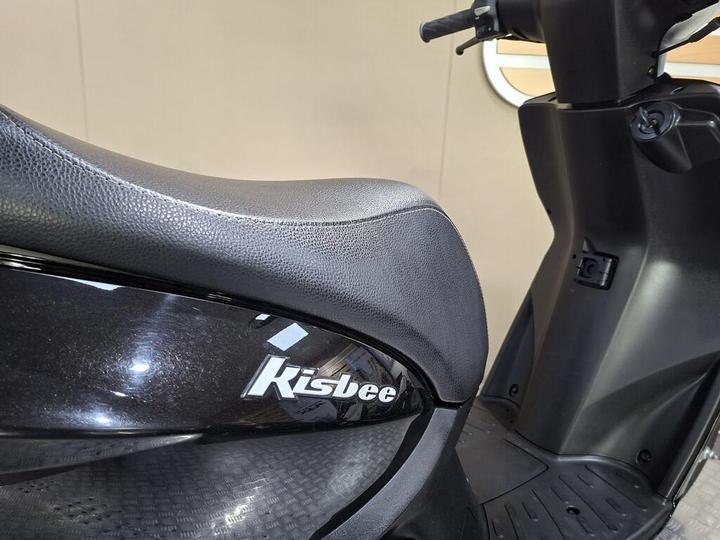 Close-up of a black scooter seat with the brand name "Kisbee" visible, against a neutral background.