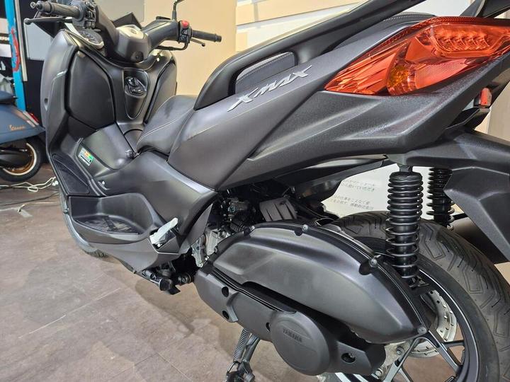 A close-up view of a black Yamaha XMAX scooter, highlighting its seat, body design, and rear suspension system.