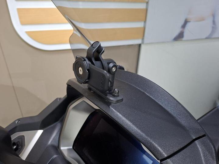Close-up of a motorcycle mount attached to the windshield, featuring a circular mechanism for securing accessories.