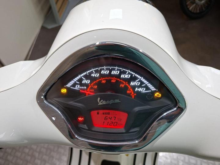 Close-up of a Vespa scooter dashboard, displaying speedometer, odometer reading of 647 km, gear indicator, and warning lights for oil and battery.