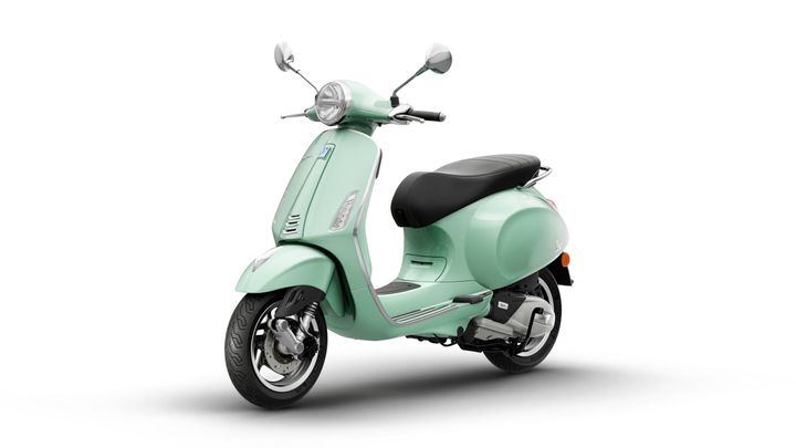 A mint green scooter with a classic design, featuring a comfortable black seat, chrome accents, and a round headlight, positioned against a white background.